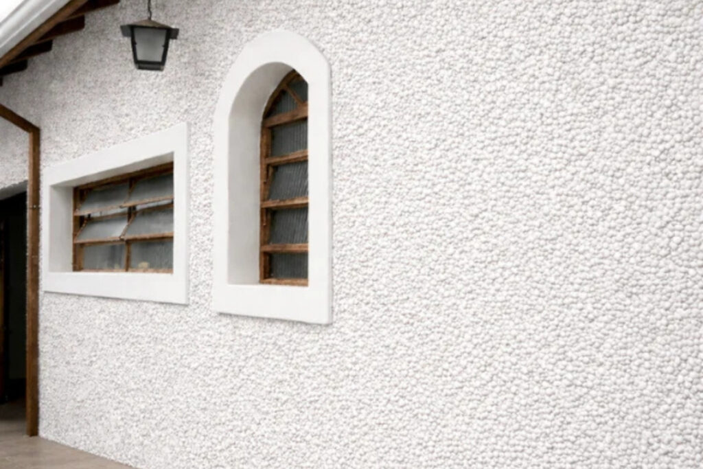 Detalhe técnico aproximado de amostra de granilha mineral natural aplicada em muro residencial de luxo na região do Tatuapé.